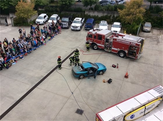 Photo from roof of fire building showing fire engine, firefighters, and a car they are practicing on